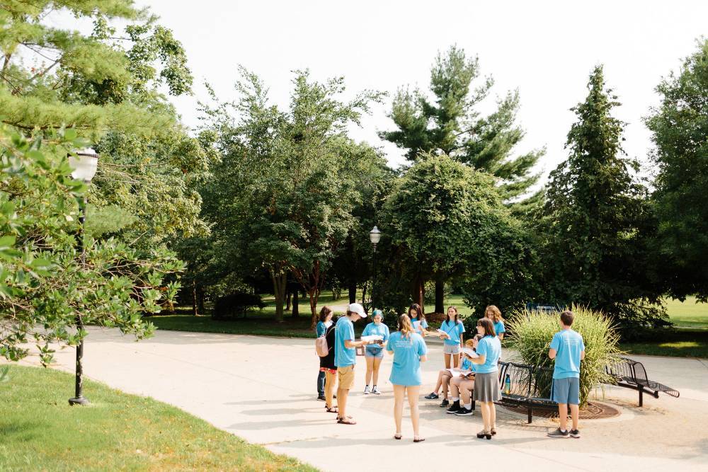 A small group of campers circle up and share their writing surrounded by trees on GVSU's campus.